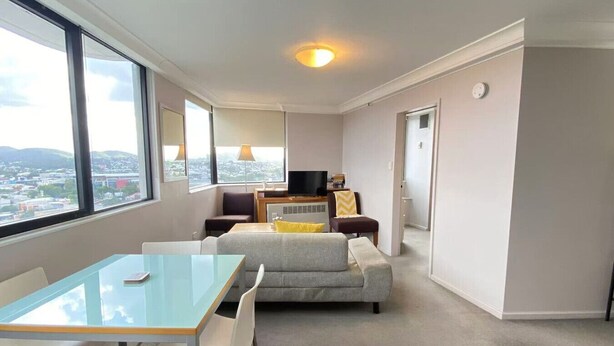 A modern living room with a glass table, grey sofa, and a TV. - PrimeCozy & Bright 1BR Apartment (Brisbane City)