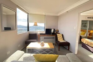 A compact hotel room with a sofa, a small table, a TV, and a chair.