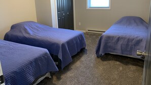 Une chambre avec deux lits, des murs de couleur beige, une fenêtre et une porte.