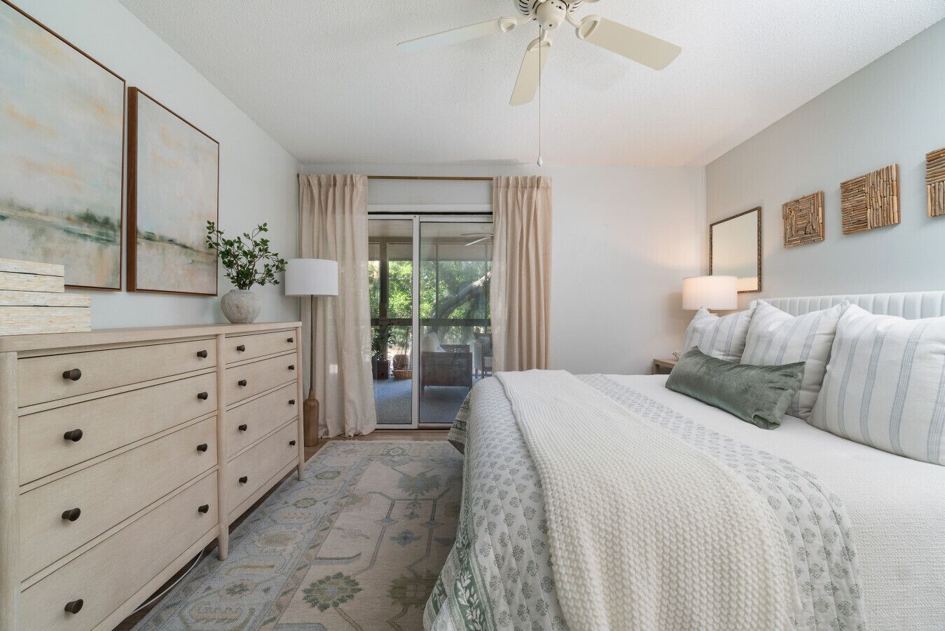Une chambre à coucher comprenant un lit, une commode et donnant sur l’extérieur grâce à une porte coulissante.