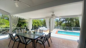 A covered outdoor dining area with a pool view, featuring a table with chairs and a ceiling fan. - Three Bed Villa with Private Pool Set In Tropical Gardens. (Harbour View Jolly Harbour)