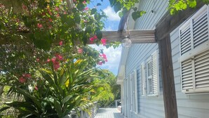 A wooden deck with a railing, leading to a white building with shutters. - Three Bed Villa with Private Pool Set In Tropical Gardens. (Harbour View Jolly Harbour)