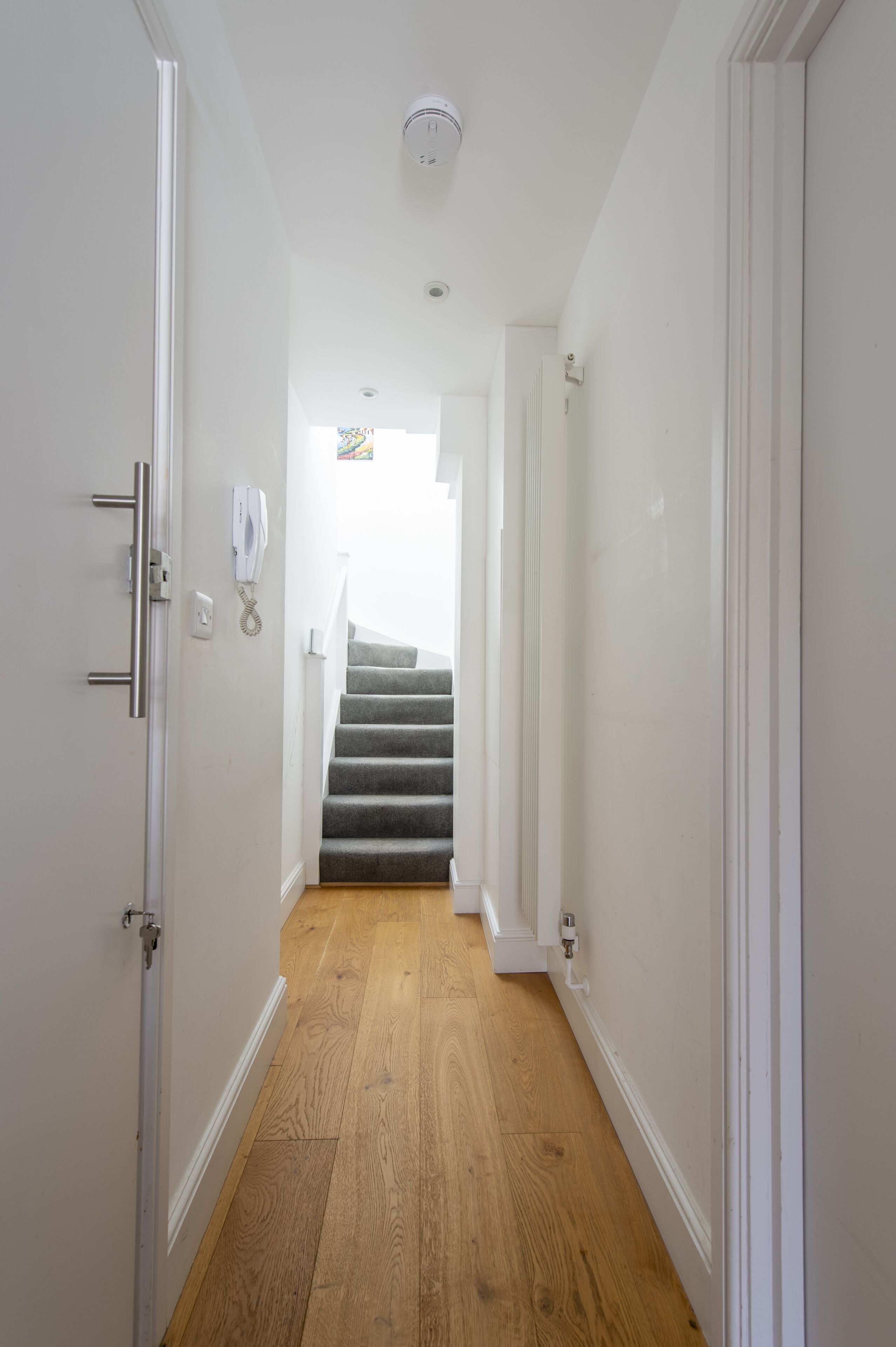 A hallway with wooden flooring, white walls, and a staircase leading to another room.