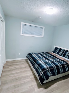 Ein Schlafzimmer mit einem Bett, einem Fenster mit Jalousien, einer Deckenleuchte und einer Tür.
