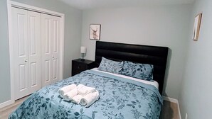 Een slaapkamer met een bed, een nachtkastje, een aan de muur hangend schilderij en een deur.