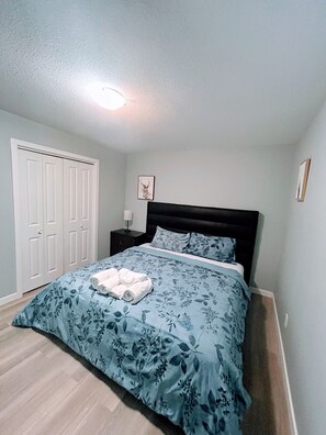 Una camera da letto con un letto, un comodino, un quadro appeso al muro e una porta.