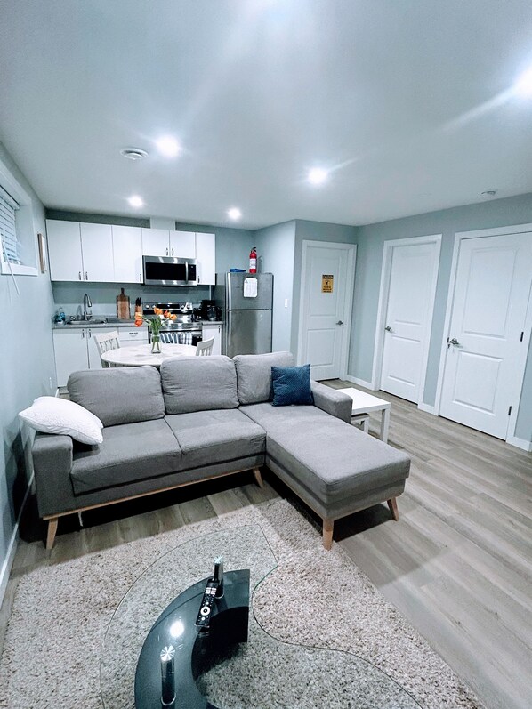 A modern living room with a grey sectional sofa, a small white table, and a remote control on a glass coffee table.
