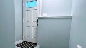 Een smalle gang met een witte deur, een klein landinrichting en een lichtschakelaar aan de muur.