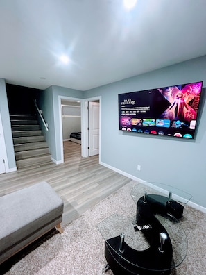 Un soggiorno moderno con una TV a schermo piatto montata a parete, un divano grigio, pavimento rivestito di moquette e una scala che conduce a un piano superiore.
