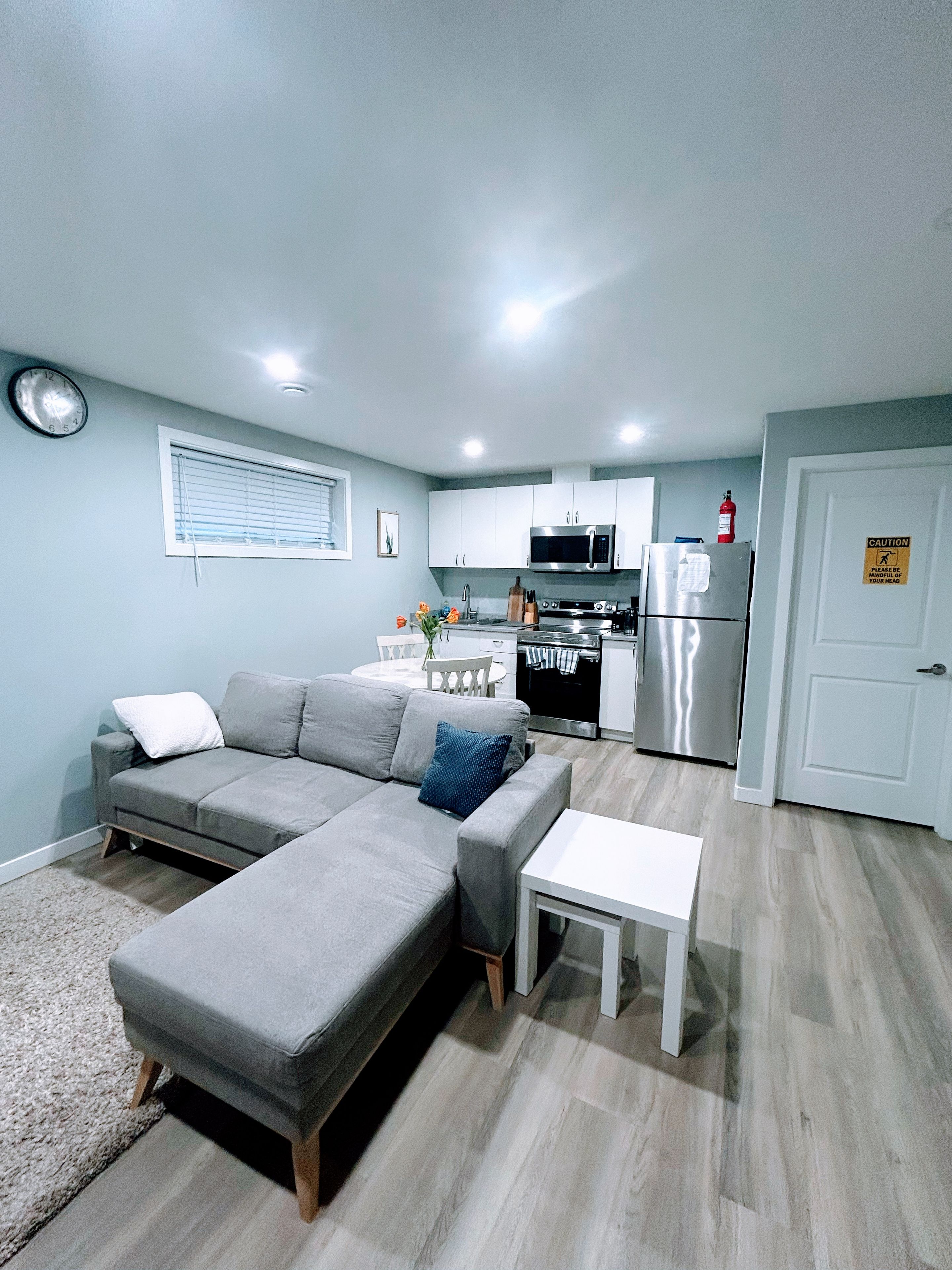 A compact living space with a sofa, a small table, a kitchenette, and a door with a caution sign.