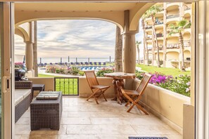 A balcony with wicker furniture, a round table, and a view of the sea and hotel buildings.
