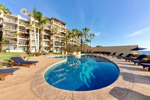 A hotel pool area with a circular pool, lounge chairs, and palm trees.