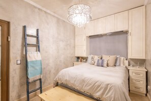 A bedroom with a bed, bedside tables, a nightstand, a chandelier, a ladder, and a bench.