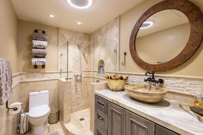 A bathroom with a stone sink, a round mirror, a shower, and a toilet.
