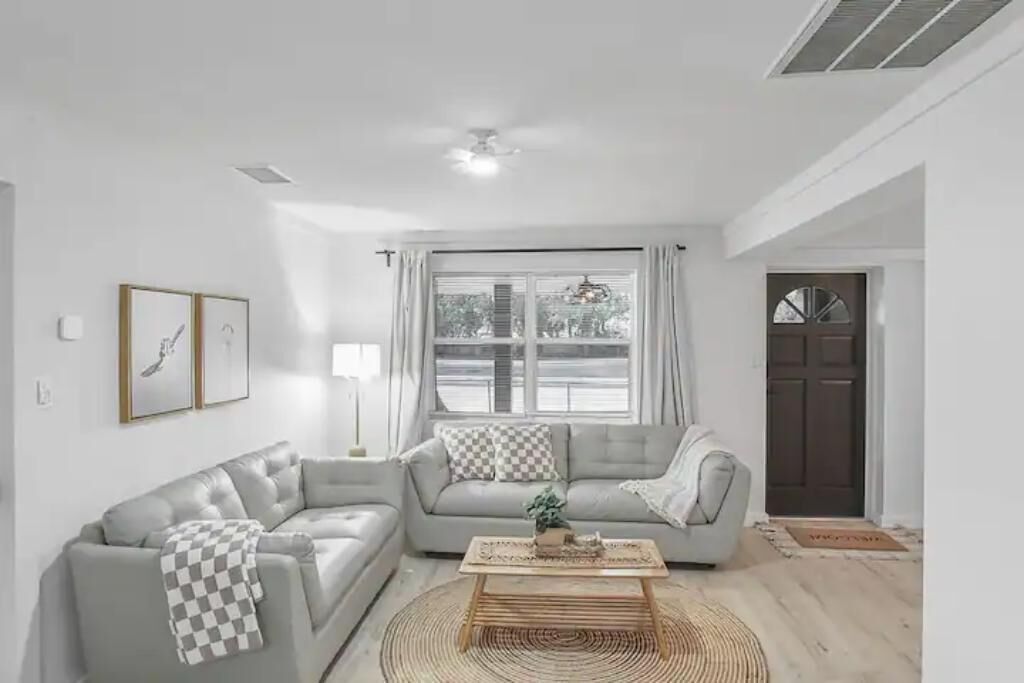 Una sala de estar moderna con un sofá gris, una mesa de centro y un ventanal con cortinas.