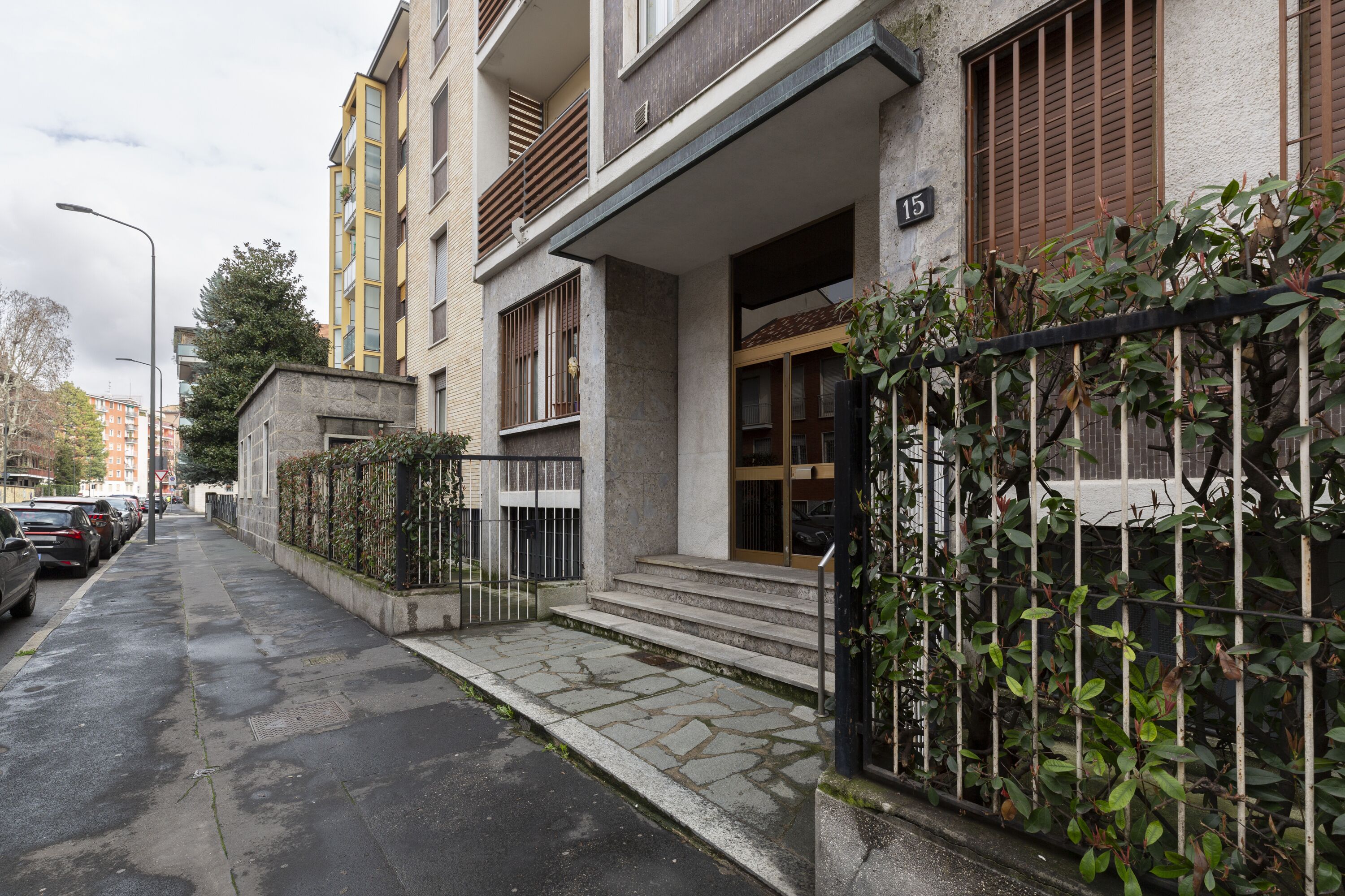 En bostadsbyggnad med en fasad av sten, en balkong och en grind vid entrén.
