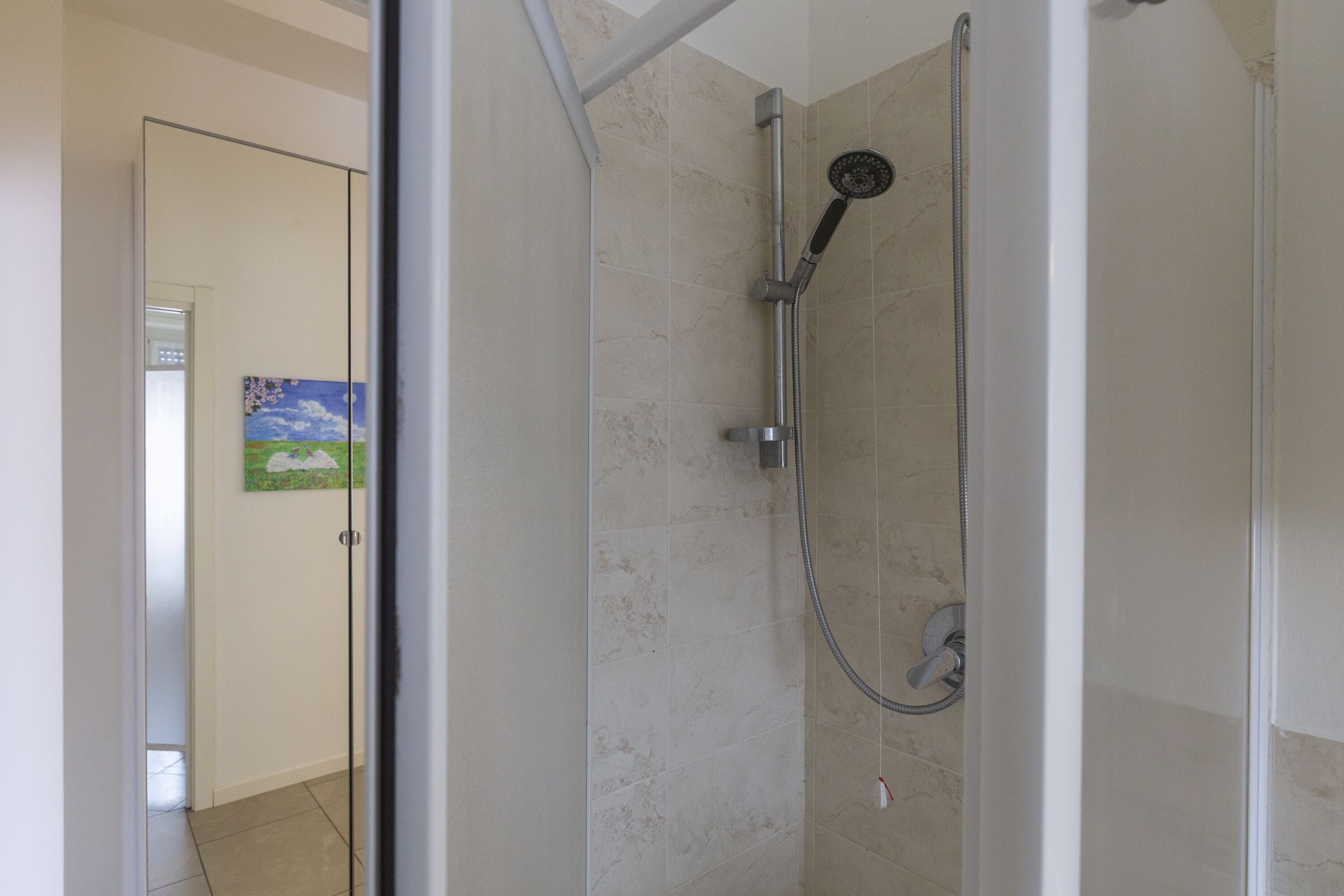 Eine begehbare, gläserne Dusche mit Handbrause und am Wand montiertem Wasserhahn.