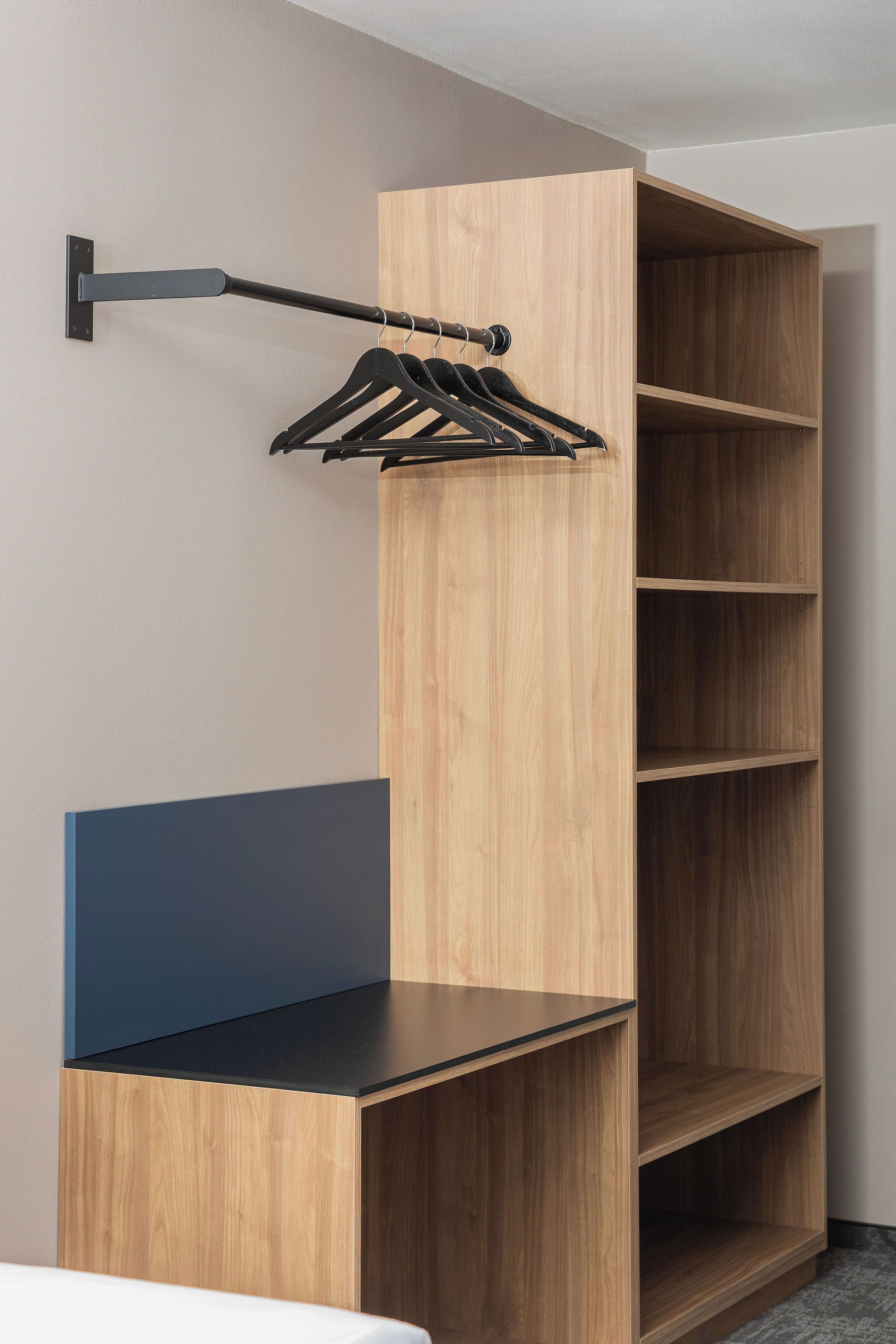 Una habitación moderna con un armario de madera, un perchero negro y un banco azul.