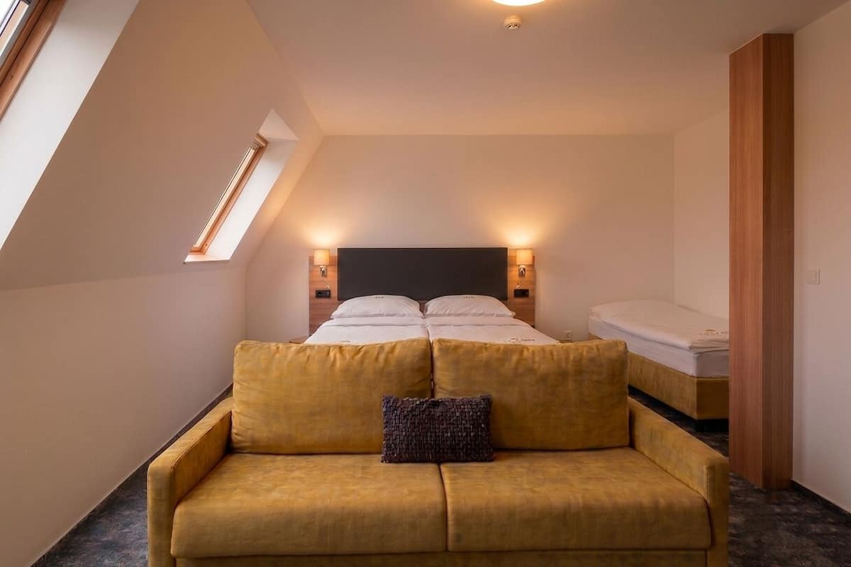 A bedroom with a bed, a sofa, a window, and a nightstand.