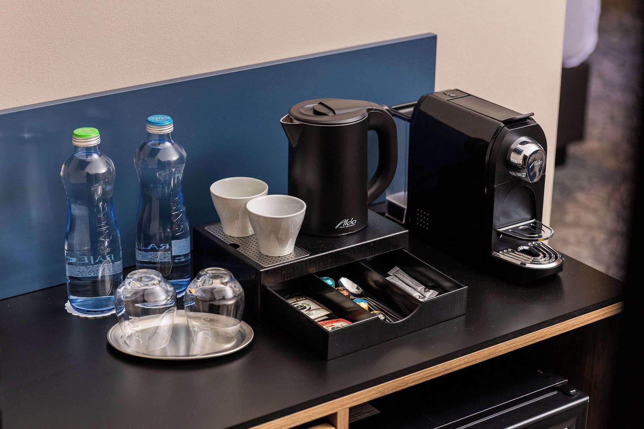 Uma estação de café com máquina de café, chávenas e garrafas de água sobre um balcão.