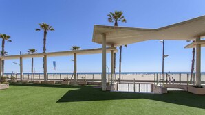 A covered outdoor area with artificial grass, palm trees, and a view of the beach.