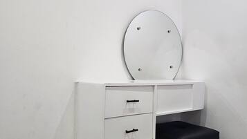 A white vanity with a round mirror and two drawers, a black stool, and a white air conditioning unit mounted on the wall.