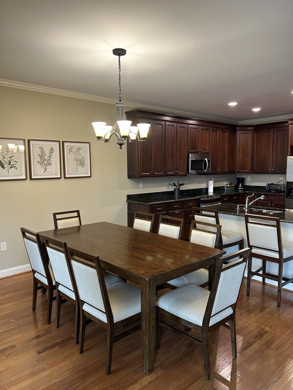 A modern kitchen with dark wooden cabinets, a central island, and a dining area with a wooden table and chairs. - The Watson Townhome in Rock Barn Country Club & Spa (Conover)