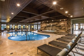 A large indoor swimming pool with a stone waterfall feature, surrounded by lounge chairs and a stone wall. - The Watson Townhome in Rock Barn Country Club & Spa (Conover)