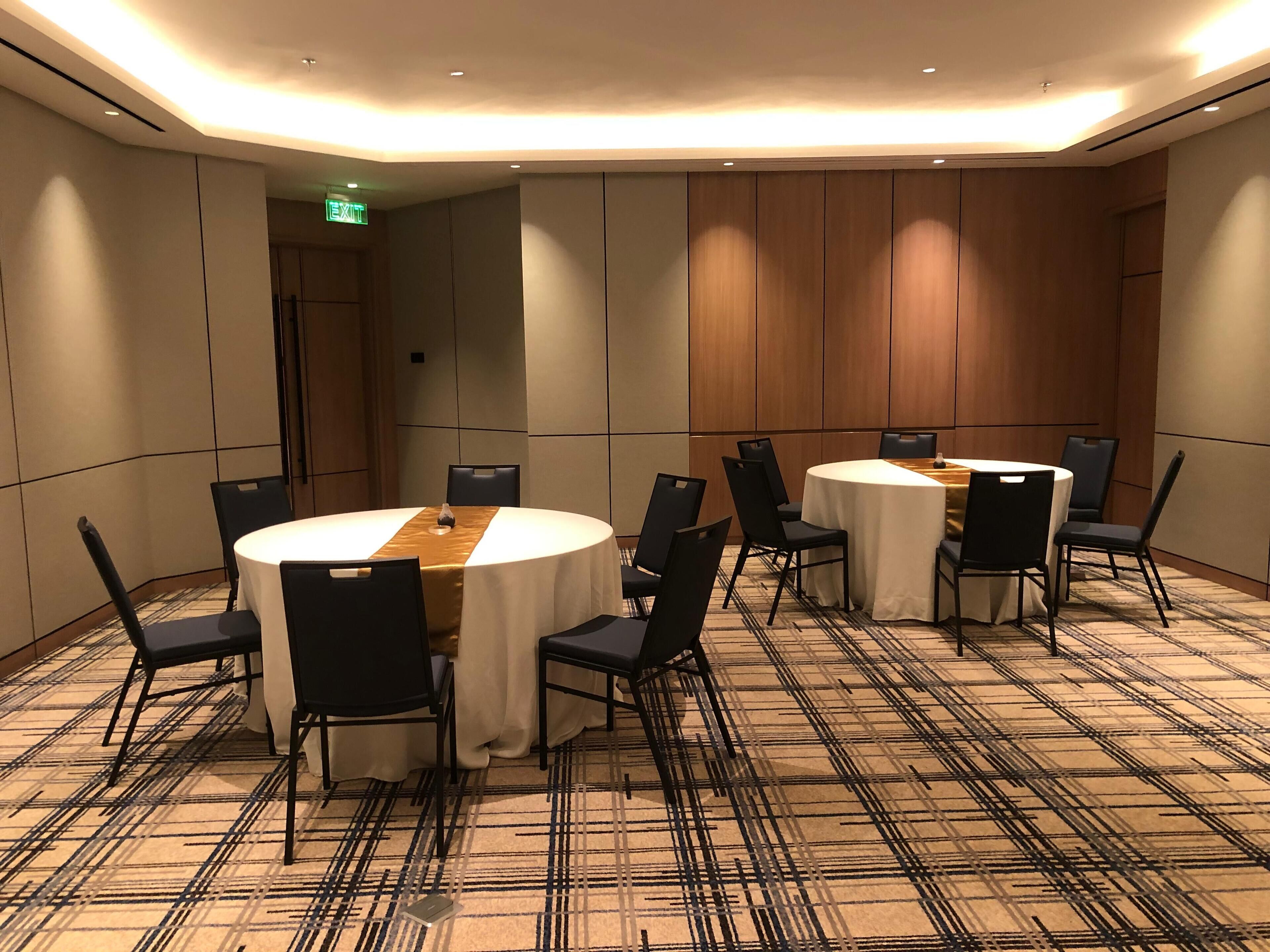 Una sala conferenze con due tavoli rotondi, sedie nere e una moquette a fantasia.