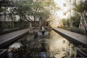 A serene courtyard with a central water feature, surrounded by lush greenery and a building facade.