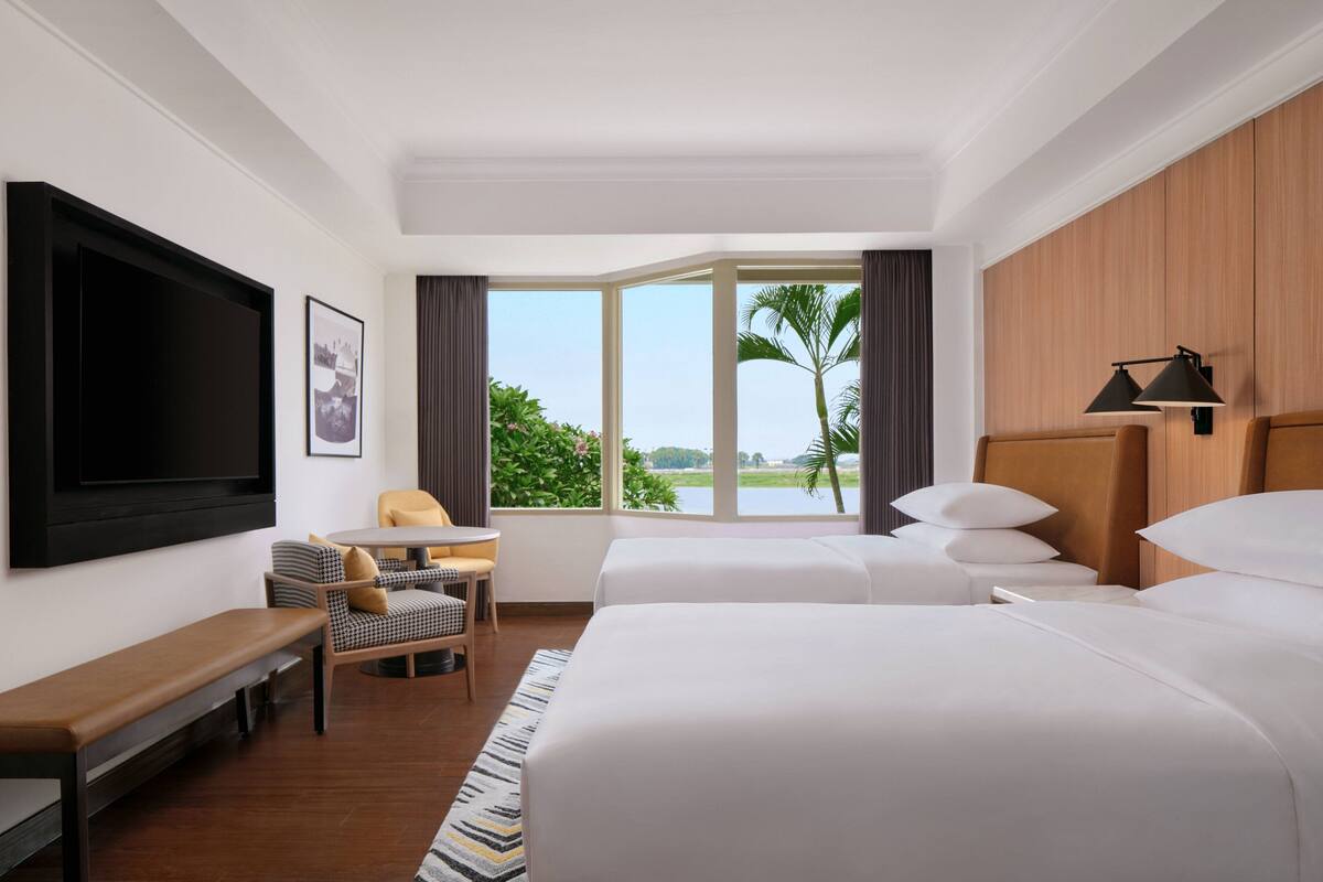 Une chambre d’hôtel avec un grand lit, un bureau, une chaise, une télévision et une fenêtre donnant sur un paysage verdoyant.
