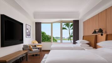 A hotel room with a large bed, a desk, a chair, a TV, and a window with a view of greenery.