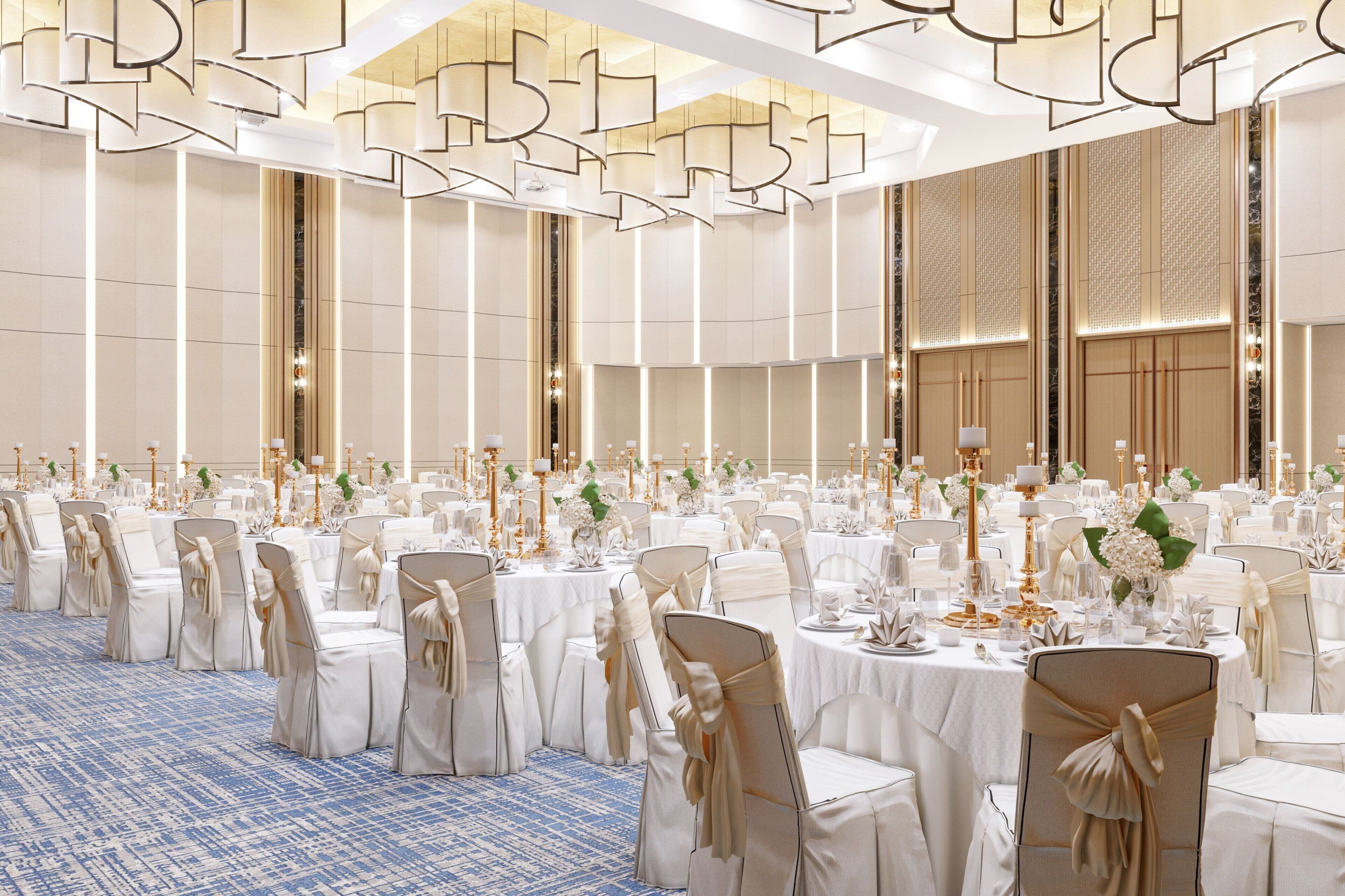 Een balzaal met rijen ronde tafels, elk gedekt met witte tafelkleden, gouden kandelaars en bloemstukken als decoratie.