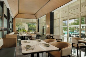 A modern restaurant with glass partitions, marble tables, and a view of a pool and greenery. - Sheraton Jakarta Soekarno Hatta Airport (Tangerang)