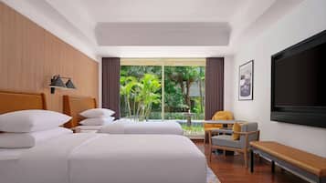Habitación de hotel con una cama grande, un escritorio, una silla, un banco, un televisor y una ventana con vistas a zonas verdes.
