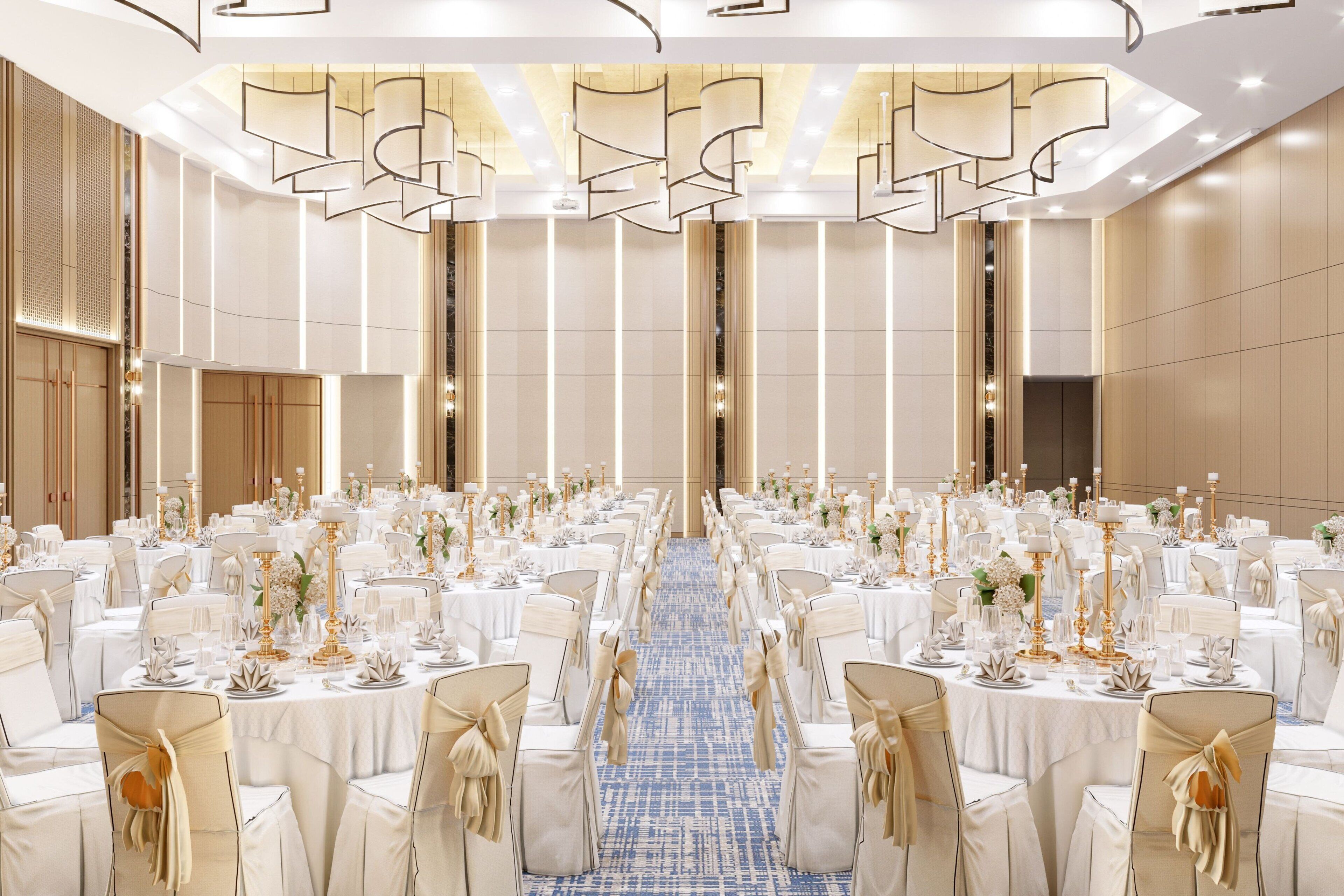 A banquet hall with rows of round tables, each set with white tablecloths, gold candelabras, and white chairs with gold sashes.
