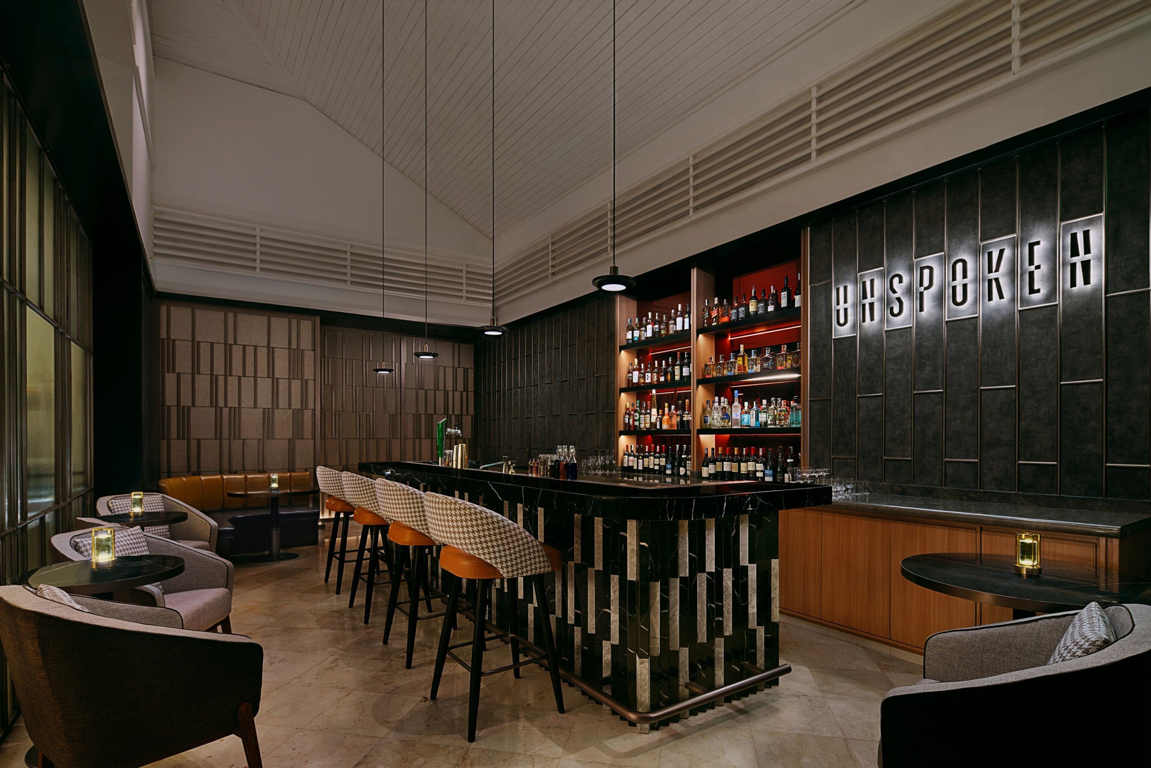 A modern bar area with a bar counter, seating, and a wall with 'UNSPOKEN' illuminated letters.