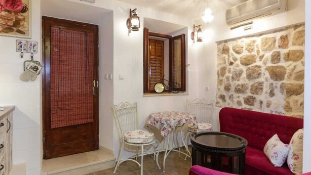 A cozy room with a stone wall, a red sofa, a small table, and a chair. - Figura suites 1 Studio in the Old town (Dubrovnik)