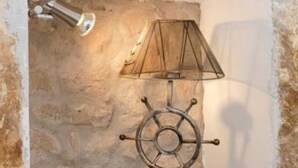 A wall-mounted lamp with a ship's wheel design, a white shelf, and a textured stone wall. - Figura suites 1 Studio in the Old town (Dubrovnik)