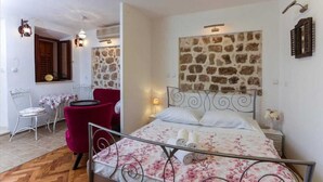 A bedroom with a stone wall, a metal bed frame, a red chair, a small table, and a lamp. - Figura suites 1 Studio in the Old town (Dubrovnik)