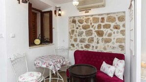 A cozy room with a stone wall, a red sofa, a small round table, and a white chair. - Figura suites 1 Studio in the Old town (Dubrovnik)