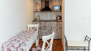 A compact kitchen with wooden cabinets, a microwave, and a dining area with a floral tablecloth. - Figura suites 2 Studio in the Old town with terrace (Dubrovnik)