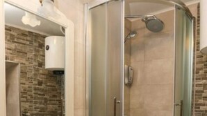 A corner bathroom with a glass-enclosed shower, a sink with a mirror above, and a brick-patterned wall. - Figura suites 2 Studio in the Old town with terrace (Dubrovnik)