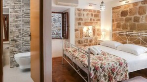 A bedroom with a stone wall, a bed with floral bedding, a nightstand, and a hanging light fixture. - Figura suites 2 Studio in the Old town with terrace (Dubrovnik)