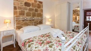 A bedroom with a stone wall, a bed with floral bedding, two bedside lamps, and a wardrobe. - Figura suites 2 Studio in the Old town with terrace (Dubrovnik)
