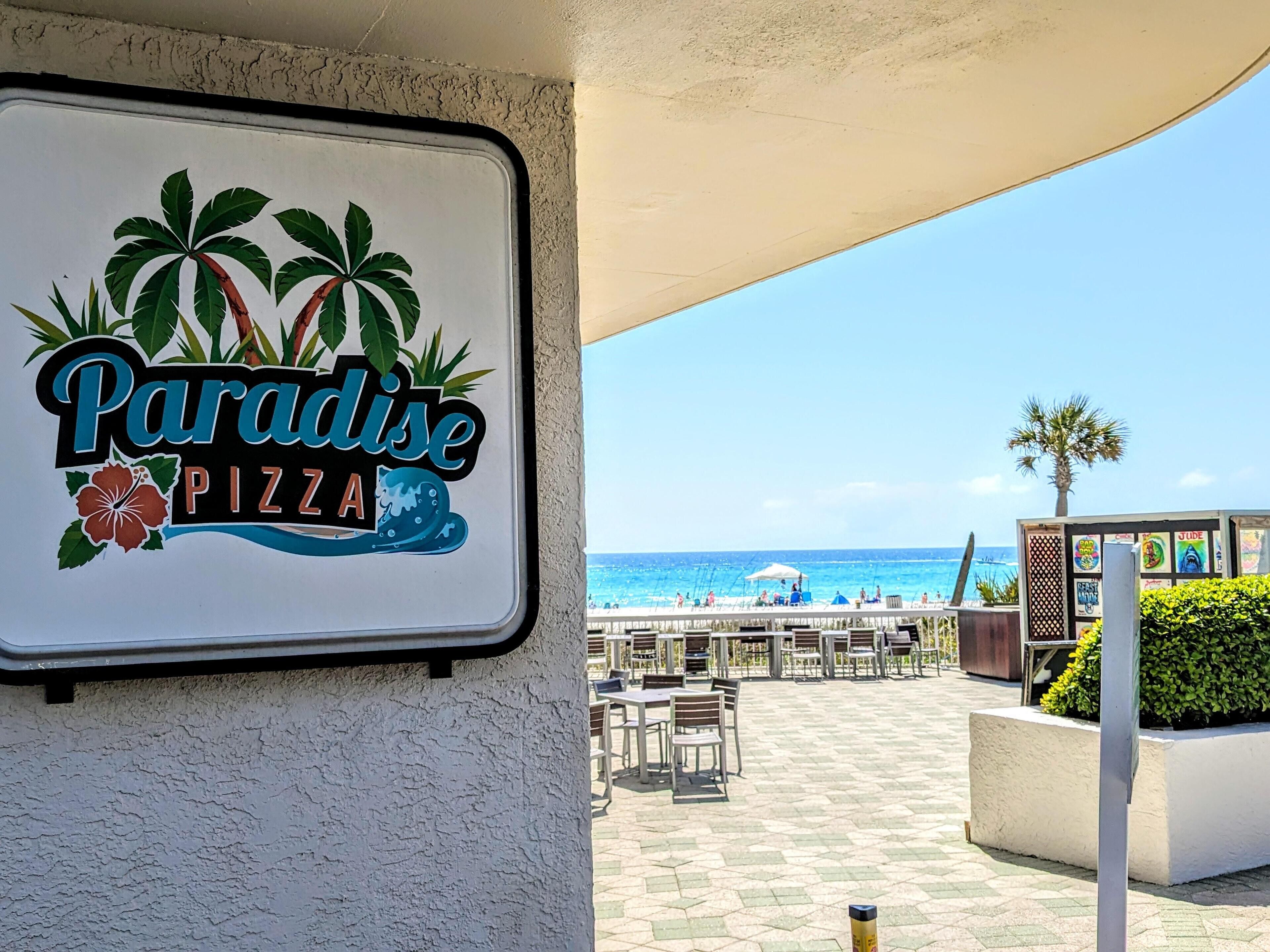 A sign for Paradise Pizza with a beach view.