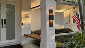 A modern building entrance with a white facade, a wooden bench, and an American flag.