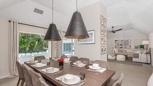 A dining area with a long wooden table set for six, two pendant lights, and a view of the outdoors.