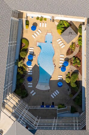 An aerial view of a hotel with a swimming pool, sun loungers, and a landscaped garden.