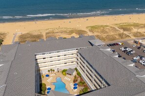 An aerial view of a hotel with a swimming pool, beach access, and a parking lot.